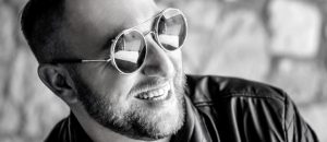 black and white photo of man with scruff and sunglasses smiling