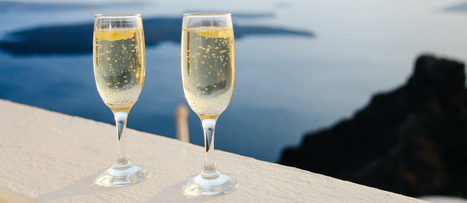 Two delicate stemmed champagne glasses perch on a railing overlooking a seascape