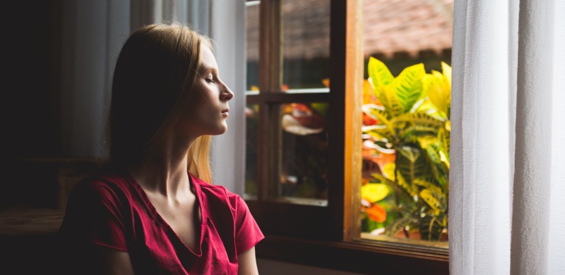 Pain-free blonde woman after root canal therapy relaxes and breathes deeply by an open window in a magenta shirt