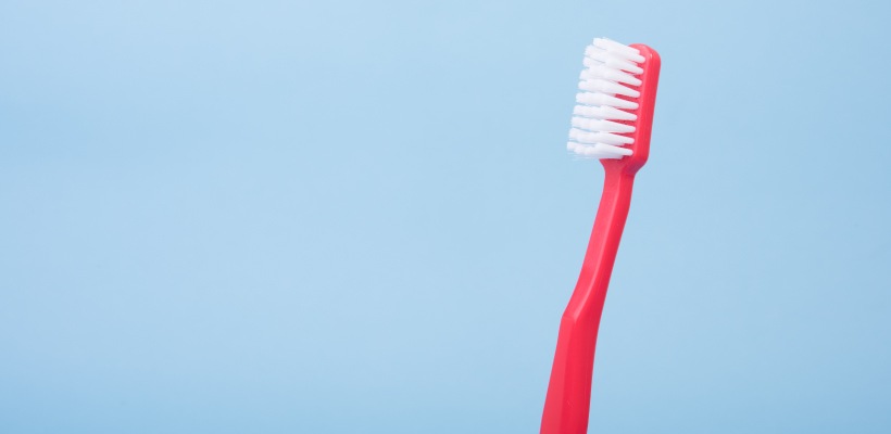Closeup of a red-handled toothbrush with white bristles against a powder blue background