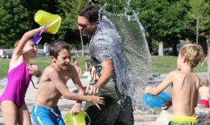 a man and three kids having a waterfight in the park