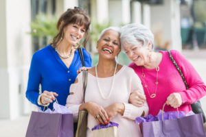 Three mature ladies laughing with arms linked carrying shopping bags