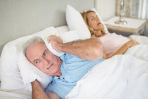 Man with a pillow over his ears while his wife snores loudly due to sleep apnea