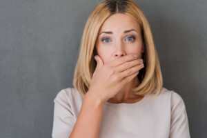 Pretty blonde woman covering her mouth for fear of bad breath