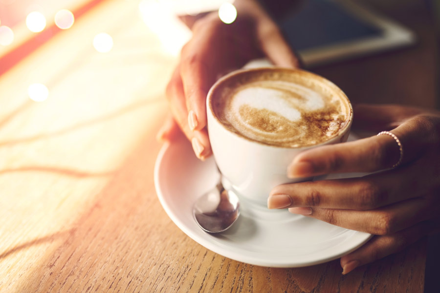 A white cup and saucer with a warm dark drink swirled with white.