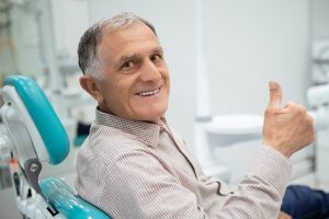 Mature man with graying hair gives the thumbs up sign while sitting in the dental chair.
