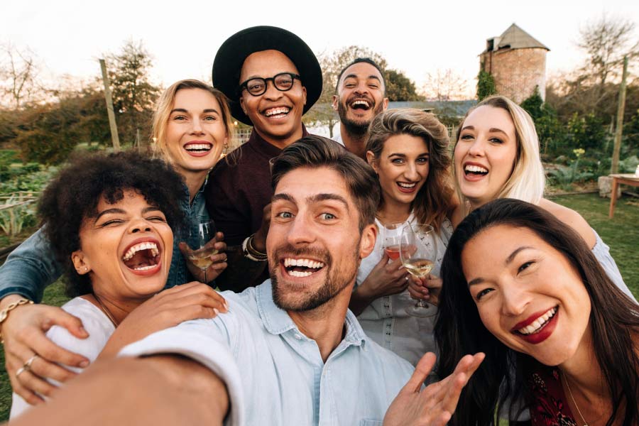 A group of smiling multicultural friends gather to take a selfie outside.