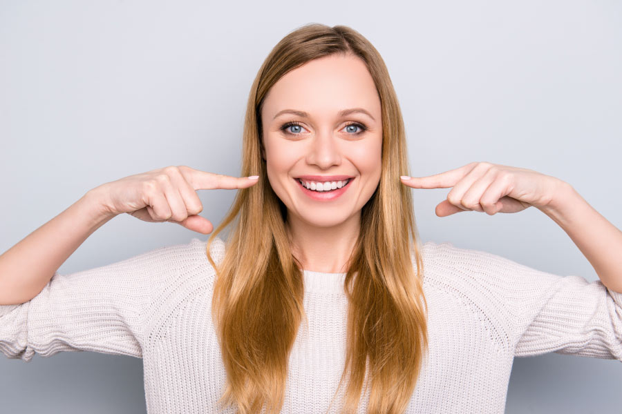 Smiling woman pointing to her professionally whitened teeth.