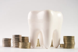 An oversized model of a tooth next to stacks of coins.