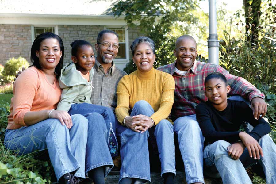 Multi-generational family sitting on the curb in front of their home.